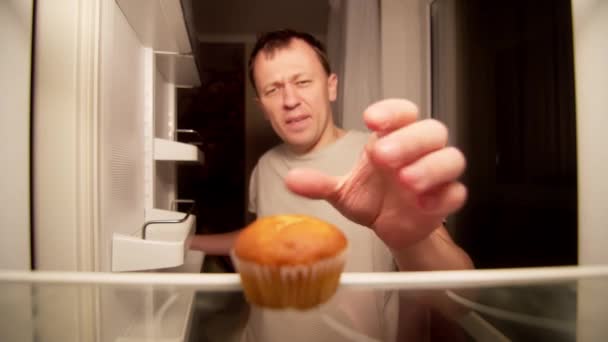 Hongerige jongeman vindt verwend cupcake in de koelkast 's nachts - Video