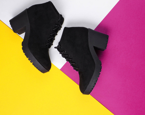 Black suede boots on a triangular colored paper background. - Фото, зображення
