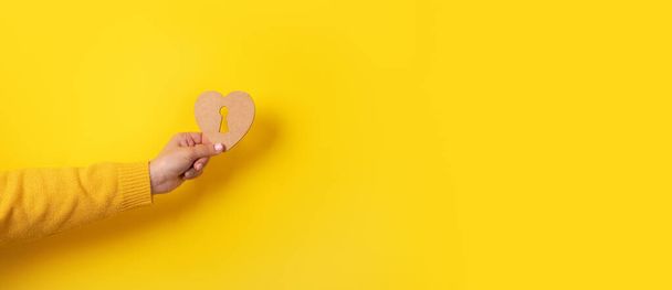 houten hart met sleutelgat in de hand over gele achtergrond - Foto, afbeelding