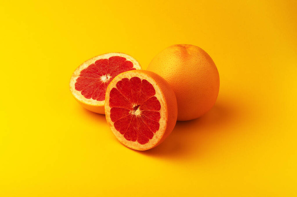 Целый и нарезанный грейпфрут на желтом фоне - Фото, изображение