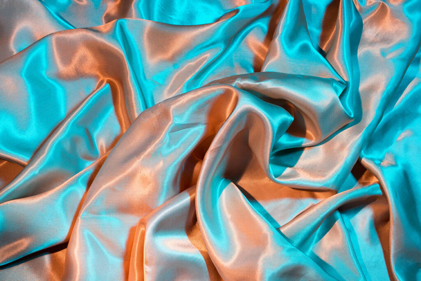 Tela suave y elegante de seda en luces azul neón y oro. Textura, fondo, espacio de copia - Foto, imagen
