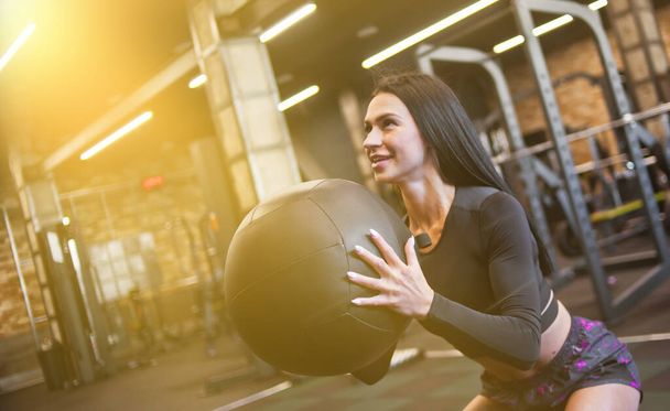 Cheerful brunette woman in sportswear doing exercise with medicine ball. - Foto, afbeelding