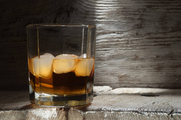 Glass of whiskey with white ice on a white wooden table - Foto, immagini