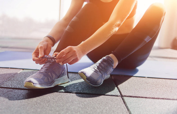 Жінка зав'язує спортивні кросівки, сидячи на килимку в спортзалі
 - Фото, зображення