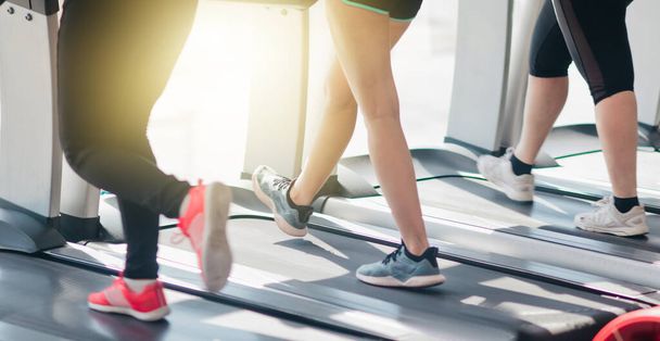 Foto recortada de piernas femeninas en ropa deportiva y zapatillas de deporte corriendo en una cinta de correr en el gimnasio contra la ventana - Foto, imagen