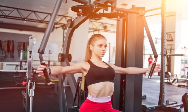 Young woman in sportswear doing exercise in exercise machine at the gym - Foto, Imagen