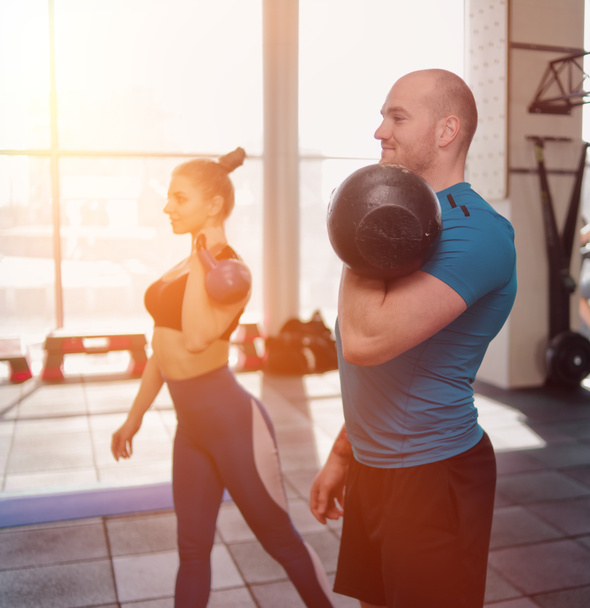 couple functional training. Sporty man and fit woman doing exercise with kettlebell in gym - Photo, Image