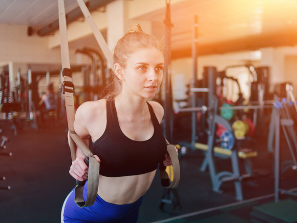 Mujer rubia joven en ropa deportiva haciendo ejercicio con correas de fitness en el gimnasio. Entrenamiento funcional - Foto, imagen