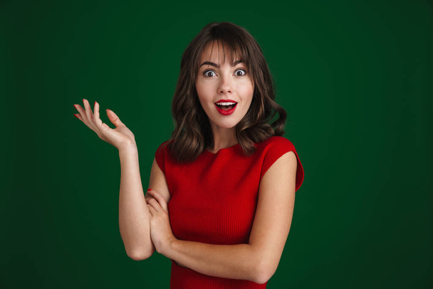 Beautiful happy brunette girl expressing surprise at camera isolated over green background - Foto, immagini