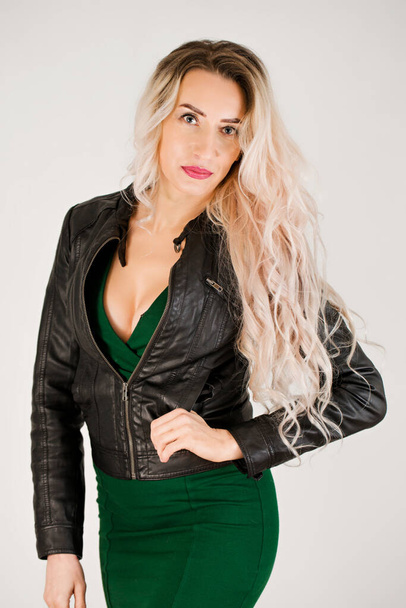 Porträt einer langhaarigen Blondine in grünem Kleid und schwarzer Lederjacke - Foto, Bild