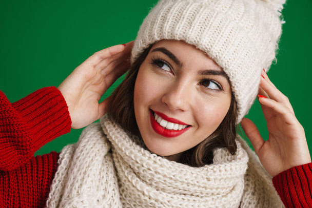 Beautiful happy girl in knit hat and scarf smiling at camera isolated over green background - Foto, immagini