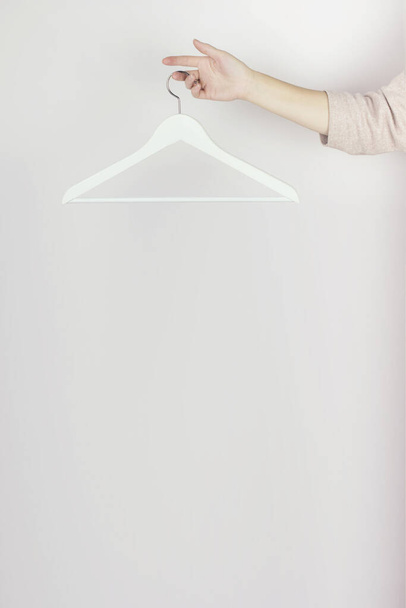 Weiße Holzbügel hängen an den Fingern, Modehintergrund. Frühjahrsverkauf Konzept Discounter Einkaufen leere Kleiderbügel - Foto, Bild