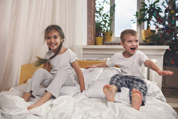 Kids in pajamas jumping in bed in the bedroom, healthy sleeping - Foto, immagini