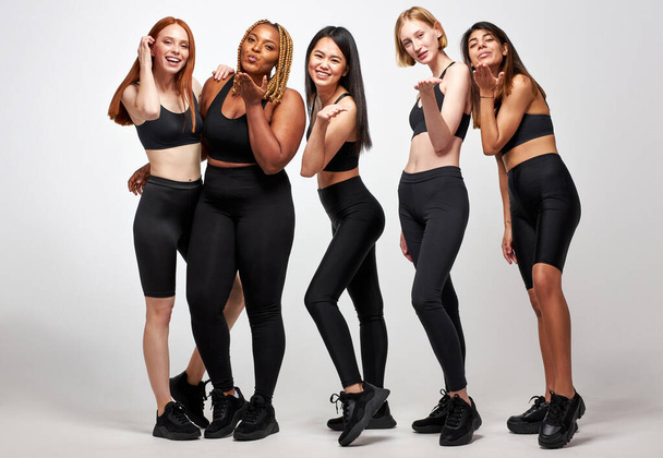 group of young diverse women in black sportive wear blowing kiss on camera - Valokuva, kuva