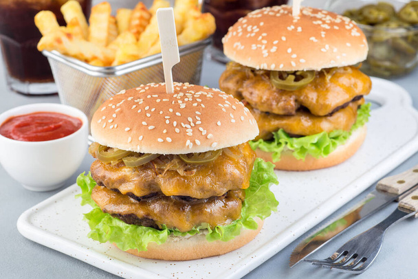 Double cheese burger with caramelized onion, lettuce and jalapeno, served with french fries and soda, on a white plate, horizontal - Photo, image