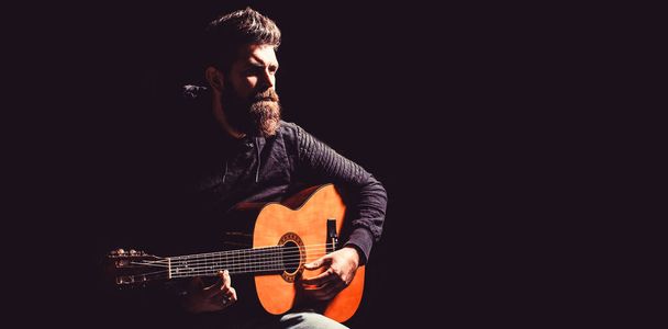 Bearded man playing guitar, holding an acoustic guitar in his hands. Music concept. Bearded guitarist plays. Play the guitar. Beard hipster man. Copy space - Photo, Image