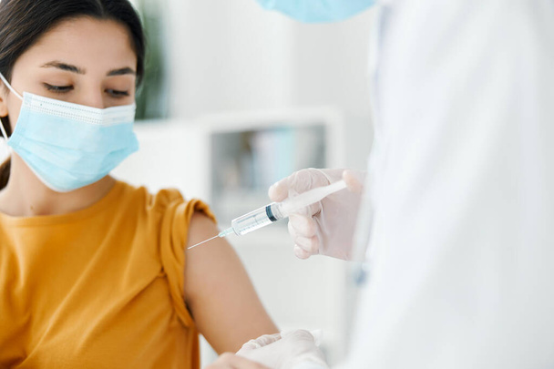 красивая женщина в медицинской маске для осмотра врачом вакцинация защитные перчатки инъекционного лечения - Фото, изображение