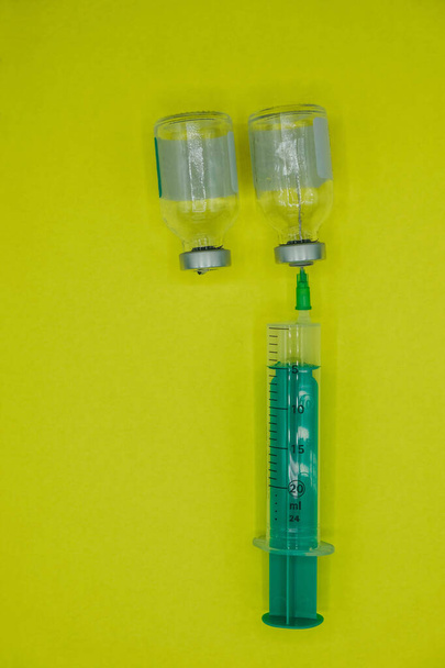 Geneesmiddel, injectie, vaccin en wegwerpspuit. Steriele flessen, ampul met aluminium dop. Gele achtergrond. Verticaal beeld. Kopieerruimte. - Foto, afbeelding