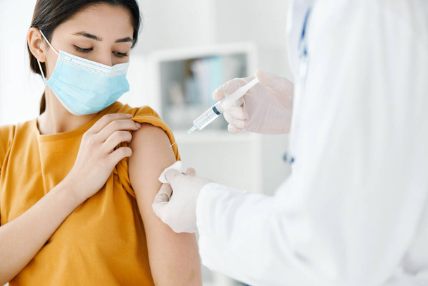 patiënt met een medisch masker kijkt naar de arts met een spuit in de hand vaccinatie - Foto, afbeelding