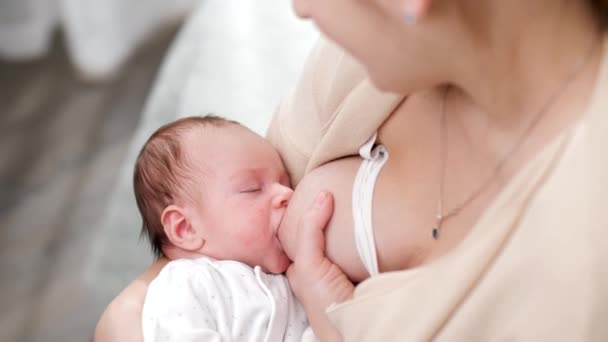 Uitzicht van bovenaf op jonge moeder kijken en schommelen haar pasgeboren baby zuigende melk uit de borst. Concept van gezonde en natuurlijke baby borstvoeding. - Video