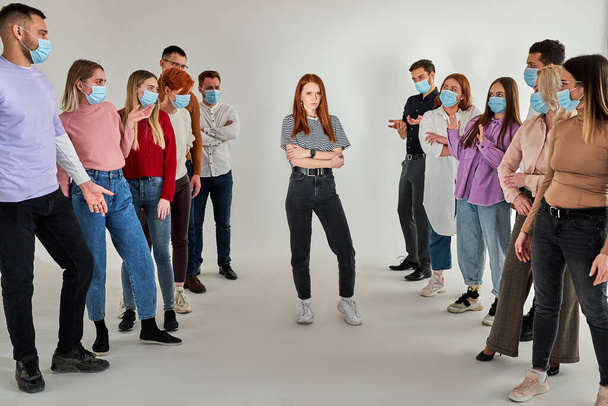 group of healthy people in medical masks avoid contact with an infected redhead woman standing in center - Фото, изображение
