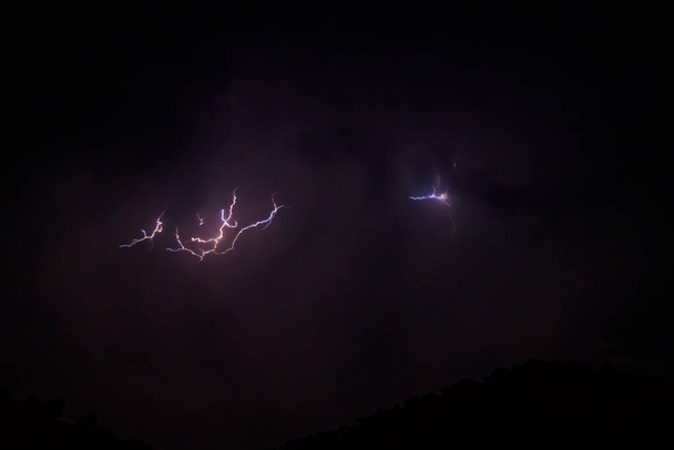 Lightning discharges in the stormy sky under dark rain clouds at night - Photo, Image