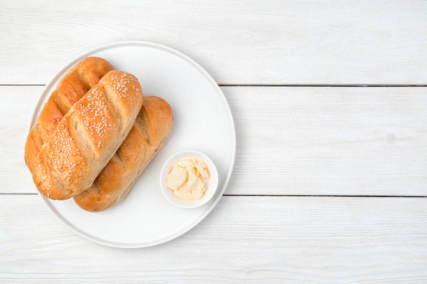 Brood en boter in een platte plaat op een witte houten ondergrond. - Foto, afbeelding