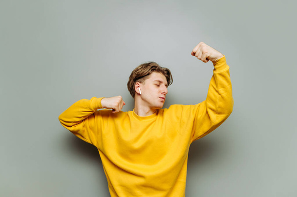 Jongeman in gele kleren danst op een achtergrond van een grijze muur in draadloze koptelefoon luisterend naar muziek. - Foto, afbeelding