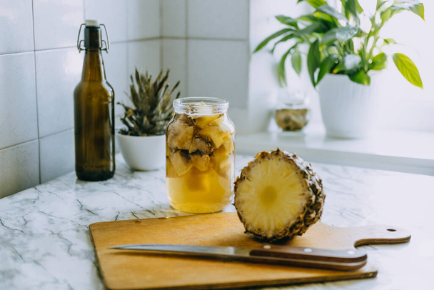 Erjesztett ananász kombucha ital tepache. Házi készítésű probiotikus szuperétel ananászos ital főzési folyamata. Igyál üveggel és szeletelt ananászt az otthoni konyhában. - Fotó, kép