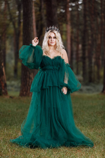 young beautiful blonde hair woman queen. Princess walks. autumn green forest mystic. Vintage medieval shiny crown. Long evening green dress. magic fantasy. - Φωτογραφία, εικόνα