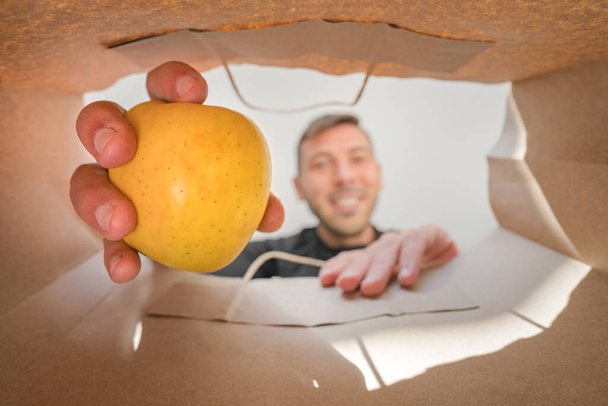 Boldog ember almát vesz ki a papírzacskóból. Házhozszállítás élelmiszerboltból karantén alatt, COVID-19. - Fotó, kép
