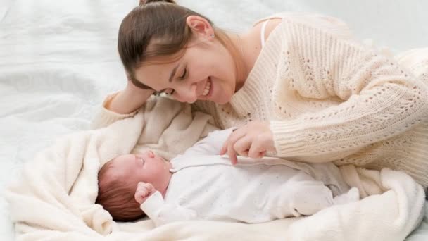 Colpo al rallentatore di felice madre sorridente che gioca e solletica il suo neonato di 1 mese sdraiato sul letto. Concetto di felicità familiare e genitori amorevoli con bambini piccoli - Filmati, video