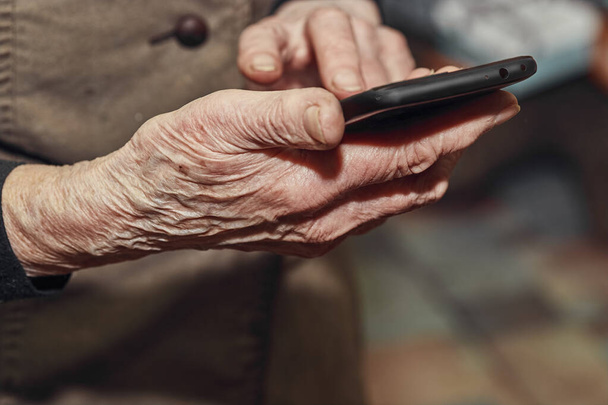 Old womans wrinkled hands hold a modern mobile phone - Фото, зображення