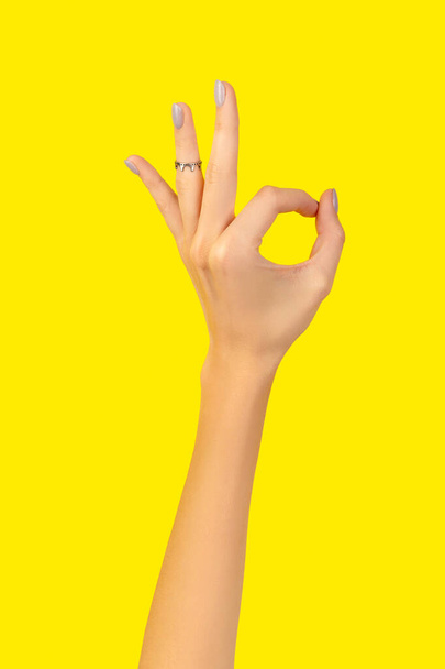 Beautiful groomed womans hand with okay gesture on yellow background - Foto, immagini