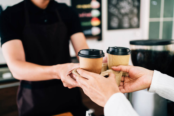 Male barista serving coffee in takeaway paper disposable cups in the coffee shop. Small green business during coronavirus pandemic.  - Photo, image