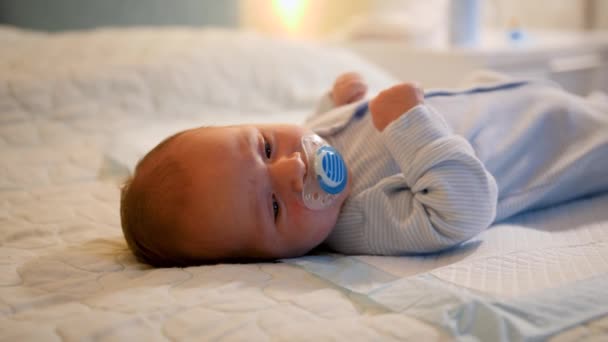Portret van pasgeboren baby die 's nachts op bed ligt en speentje of fopspeen zuigt. Begrip pasgeboren baby 's, liefhebbende en zorgzame ouders en gezinsgeluk - Video