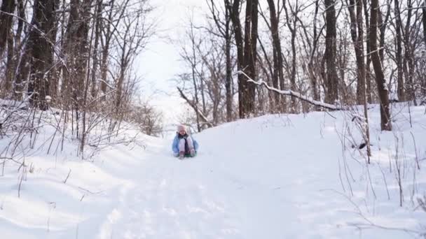 Una ragazza adolescente con un cappotto blu cerca di muoversi su una slitta da uno scivolo di neve  - Filmati, video