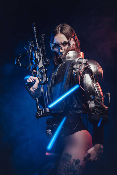 Futuristinen nainen agentti aseistettu kivääri poseeraa tumma tausta - Valokuva, kuva