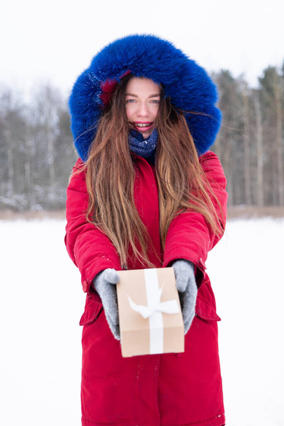 Young smiling woman in red hold gift box outdoors - Фото, изображение