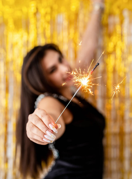 Birthday party. Beautiful young woman holding sparkler and balloon on golden background - Photo, Image