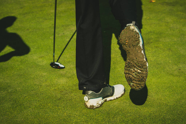 Brudne i błotniste buty golfowe na osobie trzymającej kij golfowy. - Zdjęcie, obraz
