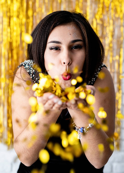 Birthday party. Portrait of young beautiful girl blowing golden confetti at holiday party - Photo, image