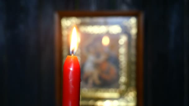Candles are burning in dark against blurred Virgin Mary icon. Religion and spirituality. Selective focus. On dark wooden wall background. Close-up. - Footage, Video