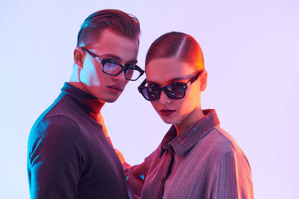 Fashion studio shot. Handsome young man and beautiful young woman posing together in stylish glasses. Optics style. - 写真・画像