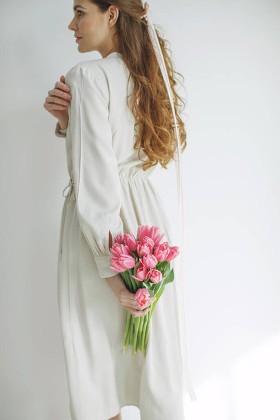 白い背景に隔離されたチューリップの花束を保持している天然生地のドレスの魅力的な若い女性. - 写真・画像