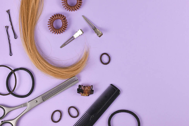 Hair styling concept with dark blond hair, elastic hair ties, hair pins, comb and thinning shears on purple background with empty copy space on side - Zdjęcie, obraz