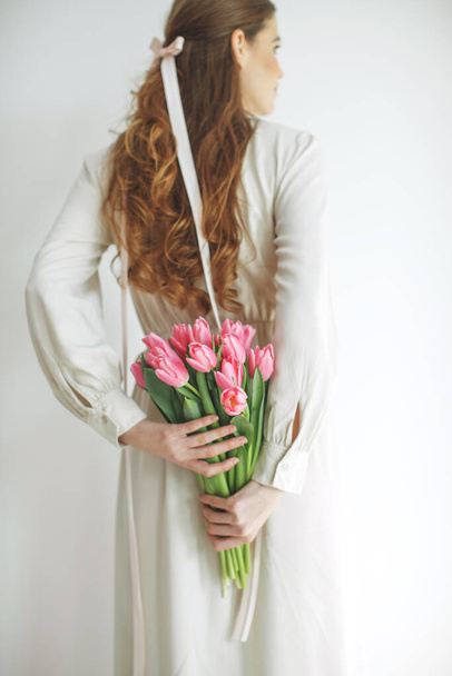 Atractiva joven en vestido de tela natural sosteniendo un ramo de tulipanes, aislado sobre fondo blanco. - Foto, Imagen