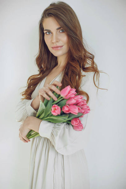 Schöne junge Frau steht isoliert und hält Tulpen. Blick in die Kamera. - Foto, Bild