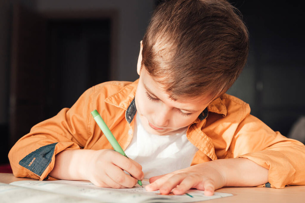 Симпатичный 7-летний ребенок выполняет домашнюю работу, сидя за письменным столом - Фото, изображение