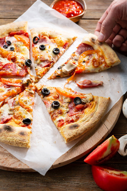 Close up of sliced pizza on cutting board, hand pull a slice - Φωτογραφία, εικόνα